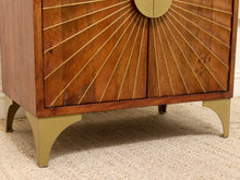 Load image into Gallery viewer, Close-up of a mid-century modern wooden cabinet with brass sunburst detailing on the doors and matching brass legs, set on a beige carpet.
