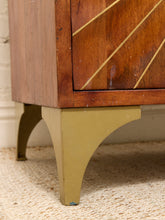 Load image into Gallery viewer, Close-up of a mid-century modern wooden cabinet or sideboard, showing a warm brown wood finish with diagonal gold-toned inlay on the drawer front and a painted olive-green curved leg.
