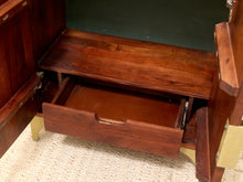 Load image into Gallery viewer, Close-up of a dark reddish-brown wooden cabinet or desk with an open drawer and a second drawer partially pulled out, showing brass hardware and a light beige carpet underneath.
