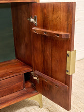 Load image into Gallery viewer, Close-up of a mid-century modern wooden cabinet with a warm reddish-brown wood finish, brass hinges, and brass legs, shown with one door swung open.
