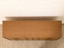 Load image into Gallery viewer, A rectangular wooden cabinet or console table with a warm medium-brown wood grain finish, shown from a top-down angle against a white brick wall and textured beige rug.
