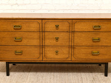 Load image into Gallery viewer, A mid-century modern wooden dresser with six drawers, featuring a warm medium-brown wood finish, brass handles, and a light beige marble top, set against a white brick wall and textured rug.
