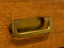 Load image into Gallery viewer, A close-up of a brass drawer pull handle mounted on a warm wood-grained surface.
