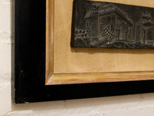 Load image into Gallery viewer, Close-up of a framed wall art piece showing a black rectangular relief plaque with an architectural scene, mounted on a beige mat inside a black frame against a white brick wall.
