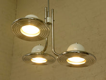Load image into Gallery viewer, A three-light chandelier with a polished chrome metal frame and white glass globes, shown illuminated against a textured beige plaster wall.
