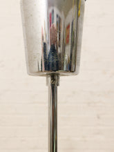 Load image into Gallery viewer, A close-up of a polished chrome metal lamp base or stand with a reflective cylindrical cup, set against a light beige brick wall.
