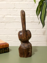 Load image into Gallery viewer, A dark brown carved wooden sculpture of a stylized face with a long nose and blocky mouth, displayed on a green tabletop against a white brick wall with a plant and books in the background.
