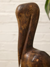 Load image into Gallery viewer, Close-up of a carved wooden pelican sculpture with a glossy dark brown finish, set against a white brick wall background.
