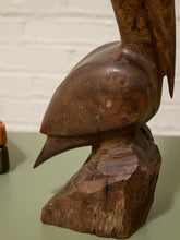 Load image into Gallery viewer, A carved wooden bird sculpture in a side profile, showcasing rich natural wood grain and textures, set against a white brick wall background.
