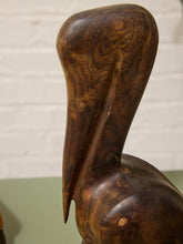 Load image into Gallery viewer, A close-up of a hand-carved wooden pelican sculpture, showcasing the rich dark brown wood grain and smooth polished finish against a white brick wall background.
