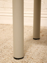Load image into Gallery viewer, Close-up of a light beige table leg standing on a textured cream rug against a white brick wall background.
