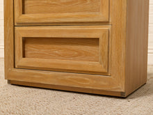 Load image into Gallery viewer, Close-up of a light oak wood chest of drawers showing the bottom drawer front, drawer frame, and base corner on a beige carpeted floor.
