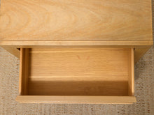 Load image into Gallery viewer, Close-up of a light natural wood drawer pulled open, showing the wood grain and interior, set against a textured beige carpet.
