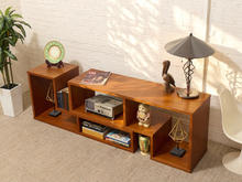 Load image into Gallery viewer, A mid-century modern wooden media console with open shelving and side cubbies, styled with books, a lamp, and decorative objects in a room with a white brick wall and beige carpet.
