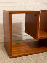 Load image into Gallery viewer, A mid-century modern wooden side table or end shelf with a warm medium-brown finish, shown in a room setting against a white brick wall and beige carpet.
