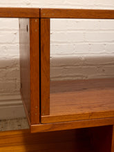 Load image into Gallery viewer, Close-up of a wooden shelf or cabinet corner with warm medium-brown wood grain, set against a white painted brick wall.
