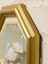 Load image into Gallery viewer, A close-up of a gold-framed art print featuring two white swans in a natural setting, mounted against a textured white brick wall.

