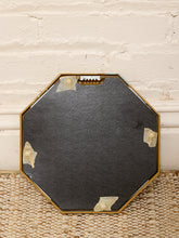 Load image into Gallery viewer, An octagonal decorative tray with a dark charcoal gray stone or slate center and a gold metal frame, resting on a woven jute rug against a white brick wall.
