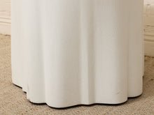 Load image into Gallery viewer, Close-up of the fluted base of a white upholstered stool or side table on a beige textured rug.
