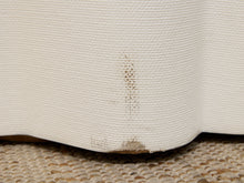 Load image into Gallery viewer, Close-up of a cream-colored textured fabric skirt or drape showing a small brown stain near the hem, resting on a woven beige surface.
