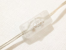Load image into Gallery viewer, A close-up of a clear plastic LED light bulb with thin metallic wire leads, resting on a textured white fabric background.
