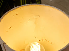 Load image into Gallery viewer, Close-up of the inside of a cylindrical lamp shade or container, glowing warm yellow under light, with visible cracks in the surface and a bulb at the bottom.
