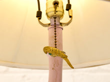 Load image into Gallery viewer, A close-up of a vintage-style lamp featuring a pale pink metal pole, a gold-toned pull chain, and a small gold bird ornament with a turquoise accent, set against a cream-colored lampshade.
