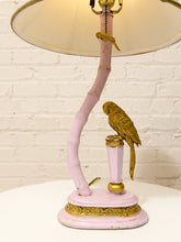 Load image into Gallery viewer, A decorative table lamp with a curved pale pink bamboo-like stem, a large cream shade, a gold-toned parrot figurine perched on the lamp base, and ornate gold detailing on a pink and gold pedestal.
