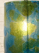 Load image into Gallery viewer, Close-up of a cylindrical product with a glossy, marbled blue and green textured finish, showing a bright light reflection in the center against a white brick wall background.
