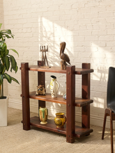 Load image into Gallery viewer, A three-tier wooden shelf with a rustic dark brown finish, styled with various decorative vases, a bird figurine, and a small animal statue in a room with a white brick wall and potted plant.
