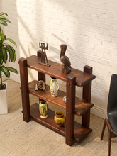 Load image into Gallery viewer, A three-tier wooden shelf with a dark brown finish, styled with various decorative vases, figurines, and a bird sculpture in a room setting with a white brick wall, beige carpet, and a potted plant.
