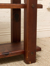 Load image into Gallery viewer, Close-up of a dark brown wooden furniture piece, showing a vertical post with a round metal screw detail, a shelf, and a horizontal support beam against a white brick wall and beige carpet.
