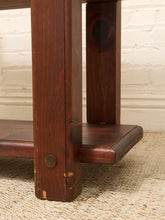 Load image into Gallery viewer, Close-up of a dark brown wooden table leg and shelf bracket with a round metal fastener, set on a woven rug against a white brick wall.
