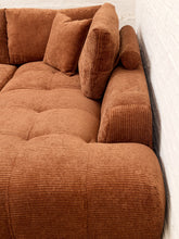 Load image into Gallery viewer, A close-up of a brown corduroy sofa with matching cushions, showing the tufted seat and ribbed fabric texture against a white brick wall.
