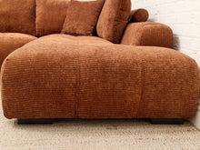 Load image into Gallery viewer, A close-up of a brown corduroy sofa with matching cushions, positioned against a white brick wall on a light beige carpet.
