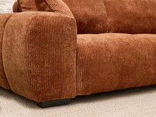 Load image into Gallery viewer, Close-up of a rust-brown corduroy sofa with a dark wooden footrest on a light beige carpet.
