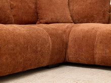 Load image into Gallery viewer, Close-up of a corner sectional sofa upholstered in a rust-orange ribbed corduroy fabric, resting on a light beige carpet.
