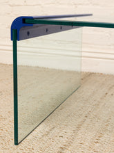 Load image into Gallery viewer, A clear glass panel with green-tinted edges and a blue metal bracket at the top, shown standing on a beige textured rug against a white brick wall.
