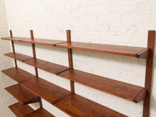 Load image into Gallery viewer, A mid-century modern wall-mounted wooden shelving unit with five tiers of warm brown wood shelves and matching vertical side supports, mounted against a white painted brick wall.
