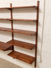 Load image into Gallery viewer, A mid-century modern wall-mounted wooden bookshelf with five tiers, made of warm brown wood, shown against a white painted brick wall.
