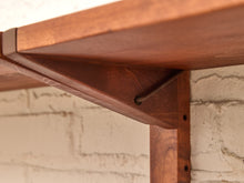 Load image into Gallery viewer, Close-up of a warm brown wooden shelf bracket mounted against a white brick wall.
