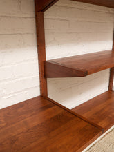 Load image into Gallery viewer, Close-up of a mid-century modern floating wooden shelf in a warm reddish-brown finish, mounted against a white painted brick wall.
