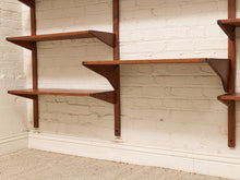 Load image into Gallery viewer, Mid-century modern wall-mounted wooden floating shelves in a warm medium-brown finish, mounted on a white-painted brick wall above a baseboard and carpet.
