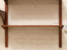 Load image into Gallery viewer, A mid-century modern wooden wall shelf with two vertical supports and a single horizontal shelf, mounted on a white brick wall.
