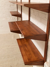 Load image into Gallery viewer, Mid-century modern floating wooden shelves in a warm medium-brown finish, mounted on a white brick wall above a light beige rug.
