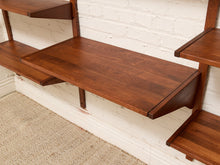Load image into Gallery viewer, A mid-century modern wall-mounted wooden shelf unit with a rich walnut finish, shown mounted on a white brick wall above a beige carpet.

