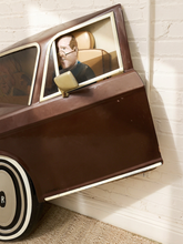 Load image into Gallery viewer, A brown vintage-style car play couch or bed with a person sitting inside, positioned against a white brick wall.
