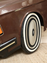 Load image into Gallery viewer, Close-up of a vintage-style brown car wheel with a cream and black tire, featuring a circular center cap with an 'R' logo, set against a beige carpeted floor.
