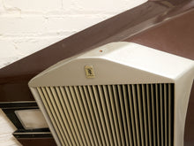 Load image into Gallery viewer, A close-up of a vintage cream-colored range hood vent with a gold-toned Rolls-Royce logo badge, set against a dark brown wooden trim and a white brick wall.
