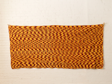 Load image into Gallery viewer, A rectangular textile wall hanging or tapestry with an abstract wavy pattern in orange, yellow, and dark red, displayed against a white painted brick wall.
